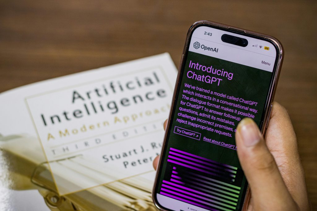 pexels-photo-16461434-16461434 Close-up of a smartphone displaying ChatGPT app held over AI textbook.